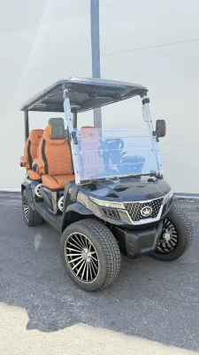 Vista frontal del un carrito de golf eléctrico dúplex con asientos de color naranja y vidrio de protección en la parte frontal.
